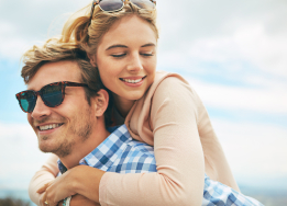 Man in sunglasses giving woman piggyback ride outdoors