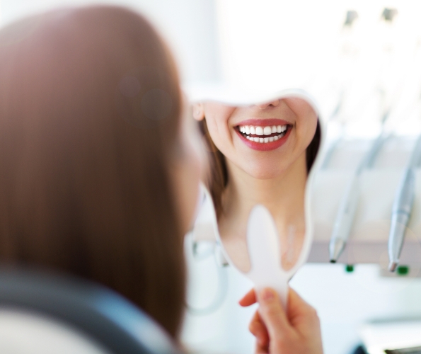 Dental patient looking at her smile in a tooth shaped mirror
