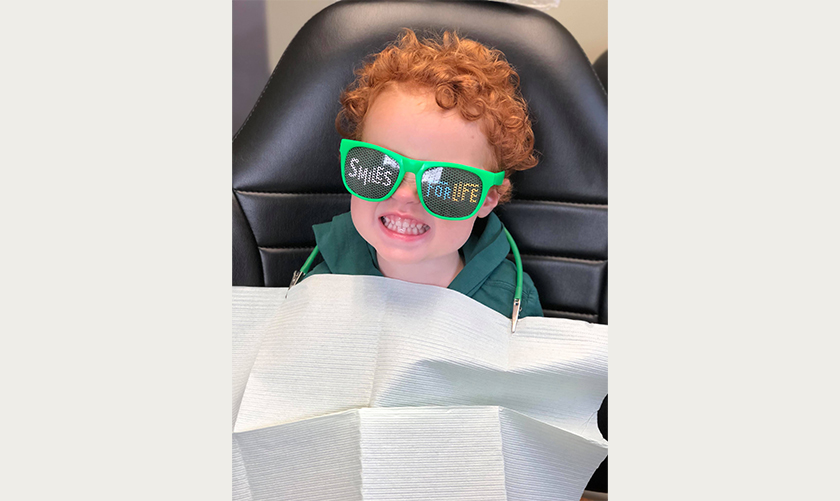 Child in dental chair wearing sunglasses that say Smiles for Life