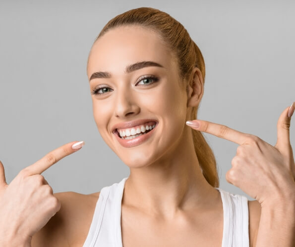 Woman with blonde ponytail pointing to her smile