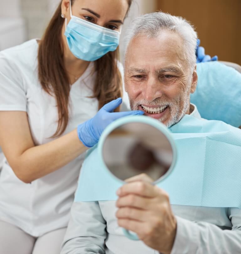 Senior dental patient looking at his smile after replacing missing teeth in Falmouth